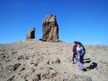 Rear view of people standing on rock formation against clear blue sky