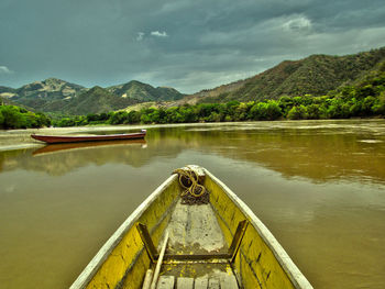 Cropped image of wooden boat in river against cloudy sky