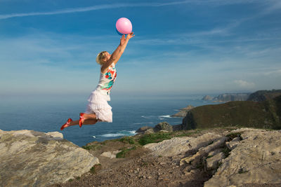 Full length of woman with balloons jumping against sky