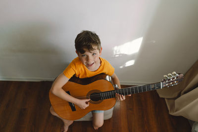 Cute boy learns to play the classical guitar in home. cozy home.