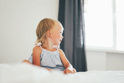 Girl looking away while sitting on bed