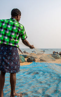 Rear view of man standing on beach against clear sky