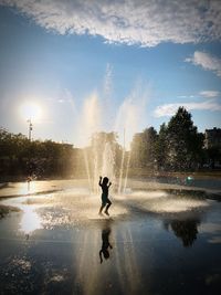 Girl playing in fountain against sky