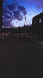 Empty road by buildings against sky at dusk