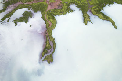 Drone view of rough rocky brown formations surrounded by lush green plants covered with thick fog in nature of iceland