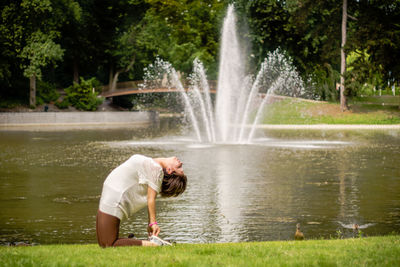 Side view of woman practicing yoga while bending against fountain in park