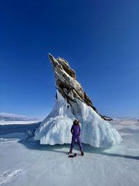 Girl standing in snow against blue sky