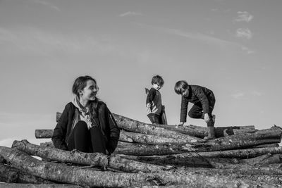 Children sitting on logs against sky