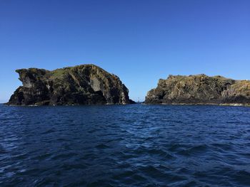 Rock formations in sea against clear blue sky