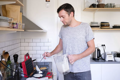 Man pouring batter on waffle iron at kitchen counter