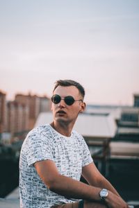 Young man wearing sunglasses standing against sky in city