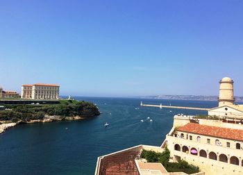 Buildings by sea against clear blue sky