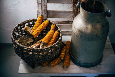 Corn in basket near metal milk jug on table