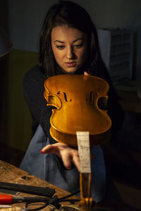 Young woman apprentice violinmaker checking the beauty of her violin