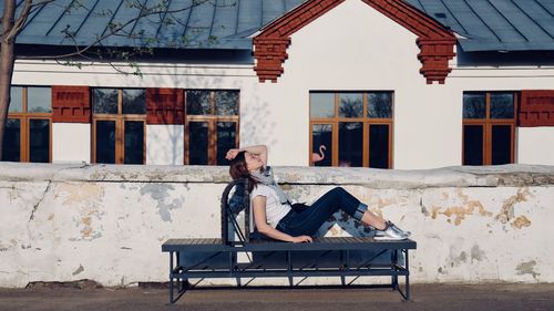 Woman relaxing on bench outside house against wall