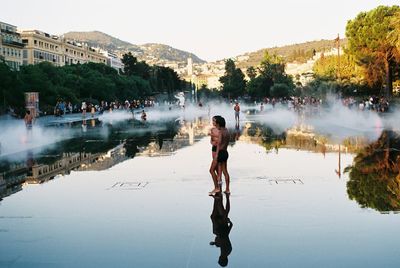 Full length of man standing by lake in city against sky