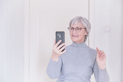 A gray-haired senior woman with glasses shopping online by mobile phone at home