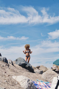 Full length of shirtless man on rock at beach against sky