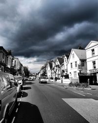 Cars on road by houses against storm clouds