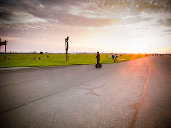 People walking on road against cloudy sky