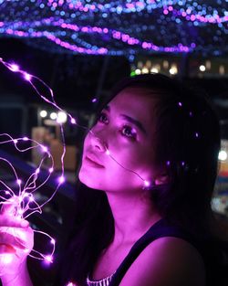 Close-up of young woman with illuminated string lights in darkroom