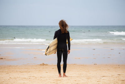 Rear view of man standing with surfboard at beach