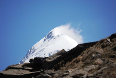 Low angle view of snowcapped mountains against clear blue sky