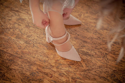 Low section of ballet dancer adjusting shoe on hardwood floor