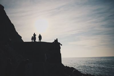 Silhouette people on cliff by sea