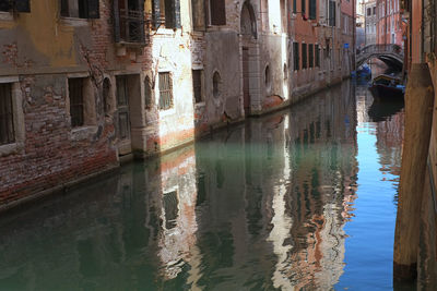 Reflection of man in canal amidst buildings in city