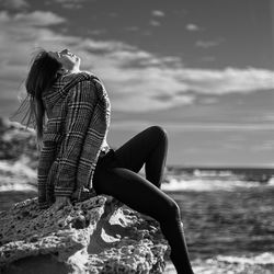 Woman sitting on rock by sea against sky