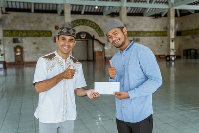 Portrait of smiling men gesturing while holding envelope at mosque