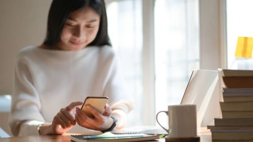 Midsection of woman using mobile phone while sitting on table