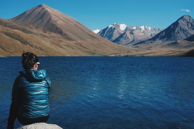 Rear view of woman relaxing on kol ukok lakeshore against mountains