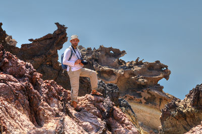 Man with camera standing on rock formation against sky