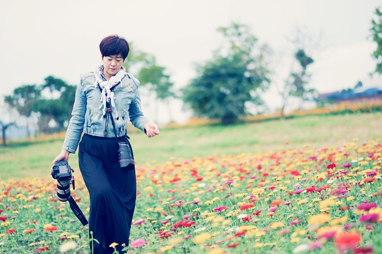 PORTRAIT OF YOUNG WOMAN WITH FLOWERS ON FIELD