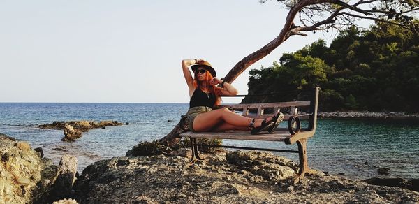 Woman sitting on beach by sea against sky