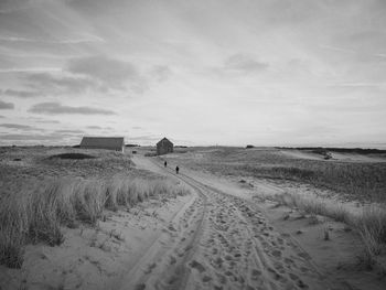 Two people walking through the dunes towards houses