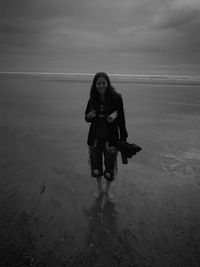 Portrait of young woman standing at beach against sky