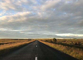 Empty road amidst field against sky during sunset