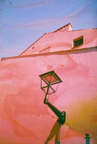 Low angle view of lamp on wall by building against sky