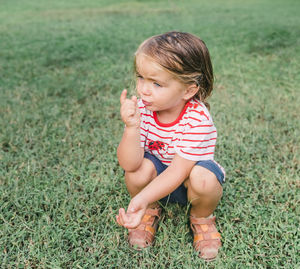 Cute girl crouching on grass while looking away