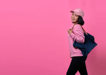 Woman looking away while standing against pink wall