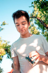 Portrait of smiling young man holding plant against sky