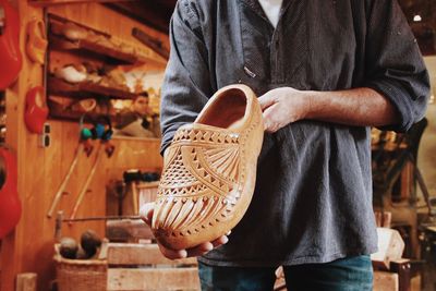 Midsection of man holding wooden shoe in workshop