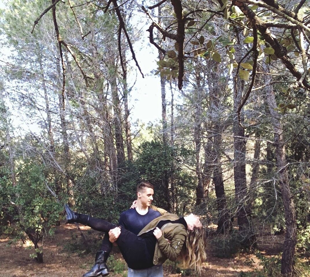 tree, leisure activity, lifestyles, young adult, person, casual clothing, forest, sitting, full length, tree trunk, young men, looking at camera, smiling, relaxation, nature, branch, vacations