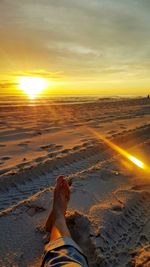 Low section of man with dog on beach against sky during sunset