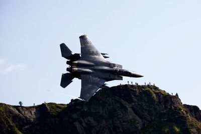 Low angle view of airplane flying over rocks against sky