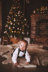 Cute baby boy crawling on floor against christmas tree at home