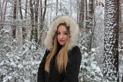 Portrait of beautiful young woman in warm clothing standing at forest during winter